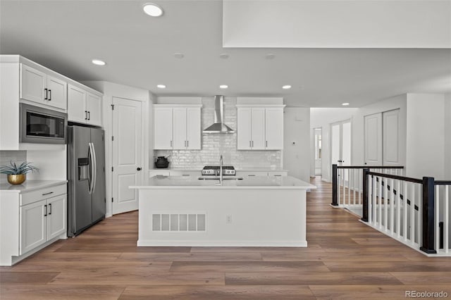 kitchen featuring built in microwave, white cabinets, stainless steel fridge, and wall chimney exhaust hood