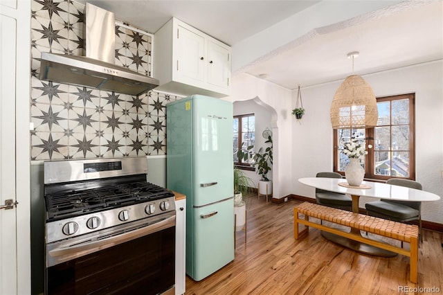 kitchen with decorative light fixtures, white cabinetry, white fridge, stainless steel gas range oven, and wall chimney range hood