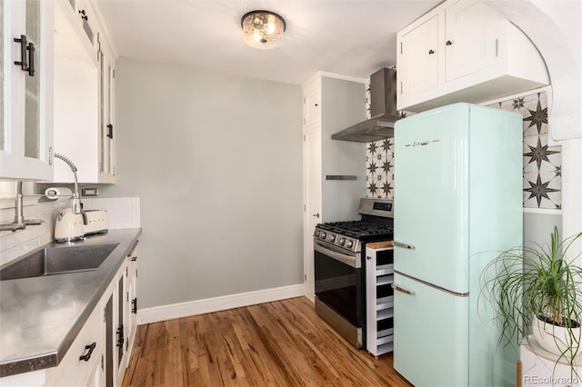 kitchen with white cabinetry, white refrigerator, gas stove, light wood-type flooring, and wall chimney exhaust hood