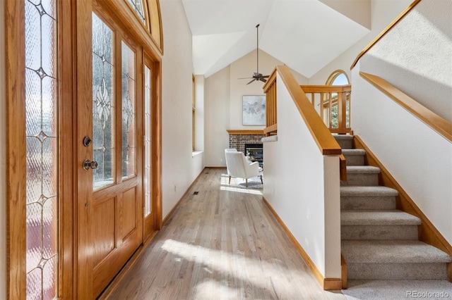 foyer entrance featuring a ceiling fan, stairway, light wood finished floors, lofted ceiling, and a brick fireplace