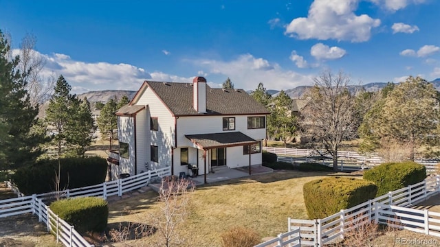 rear view of property featuring fence, a chimney, a yard, a mountain view, and a patio