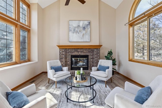 living room featuring high vaulted ceiling, wood finished floors, a fireplace, baseboards, and ceiling fan