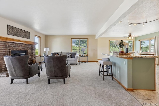 living room featuring baseboards, light colored carpet, a fireplace, a textured ceiling, and a ceiling fan