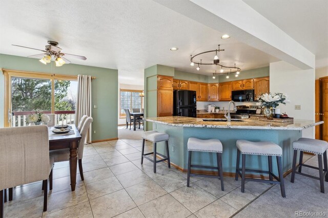 kitchen with a breakfast bar area, light stone counters, a peninsula, black appliances, and a sink