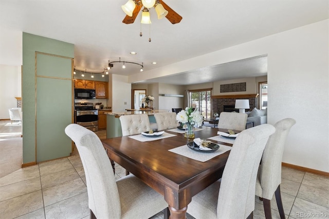 dining area featuring light tile patterned floors, a fireplace, baseboards, and a ceiling fan