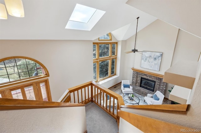 living room featuring vaulted ceiling with skylight, a healthy amount of sunlight, a brick fireplace, and ceiling fan
