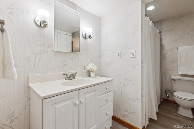 full bathroom with toilet, wood finished floors, wallpapered walls, baseboards, and vanity