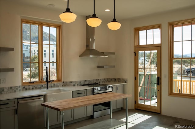 kitchen with butcher block counters, stainless steel appliances, a healthy amount of sunlight, wall chimney range hood, and a sink