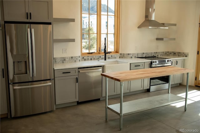 kitchen with stainless steel appliances, wood counters, wall chimney exhaust hood, a wealth of natural light, and open shelves