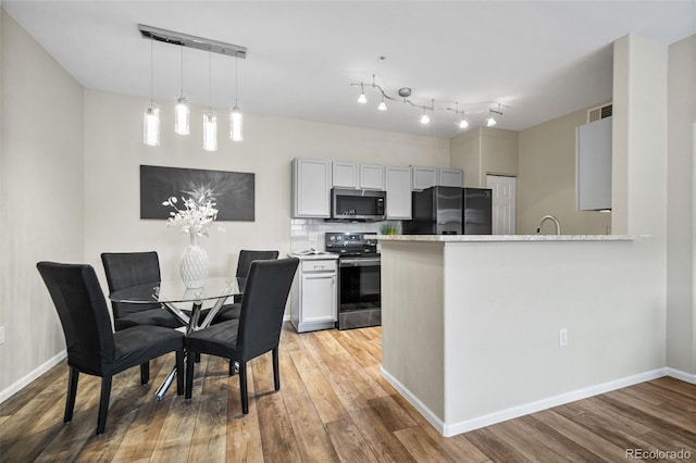 kitchen with kitchen peninsula, decorative backsplash, appliances with stainless steel finishes, decorative light fixtures, and wood-type flooring