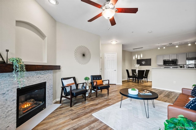 living room with ceiling fan, light hardwood / wood-style floors, and a stone fireplace