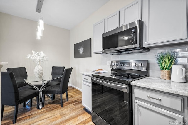 kitchen featuring pendant lighting, backsplash, light wood-type flooring, light stone counters, and stainless steel appliances