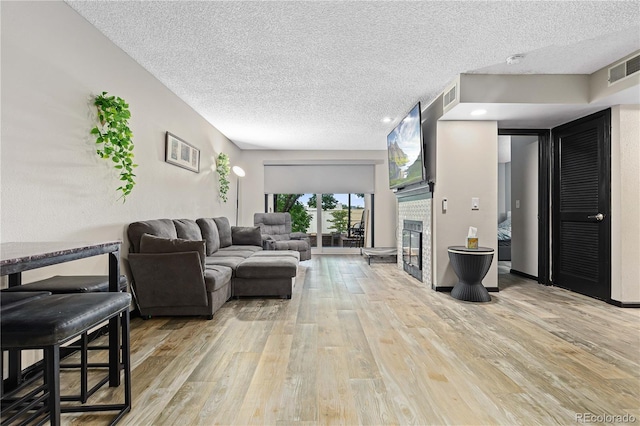 living room featuring a tile fireplace, a textured ceiling, and light wood-type flooring