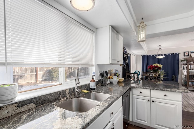 kitchen with dark stone countertops, white cabinetry, sink, and hanging light fixtures