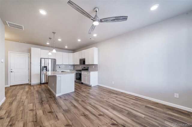 1983 S Poplar Ct, Denver, CO 80224 - kitchen with stainless steel appliances, white cabinets, light wood-style floors, a kitchen island with sink, and backsplash