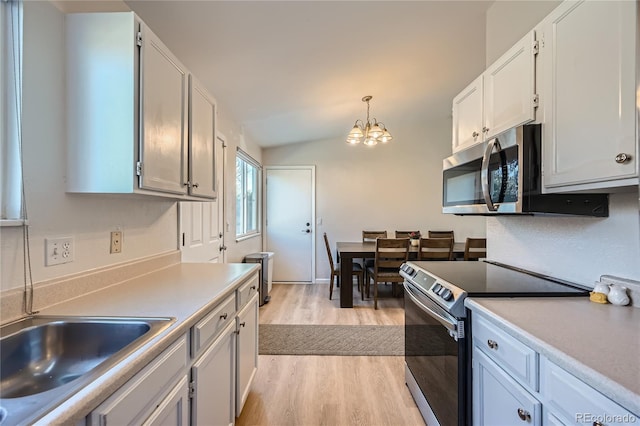 kitchen featuring hanging light fixtures, appliances with stainless steel finishes, vaulted ceiling, white cabinets, and light wood-type flooring