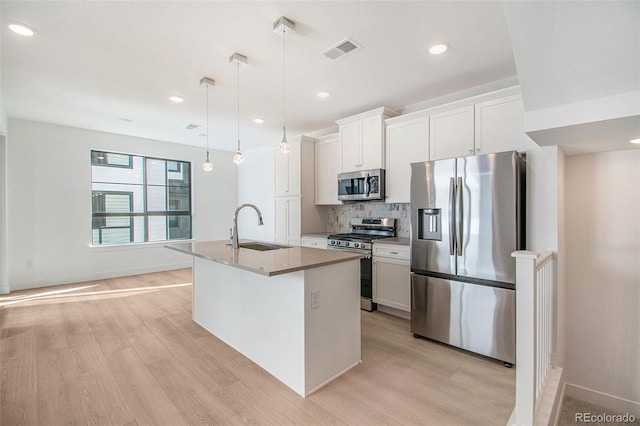 kitchen with sink, appliances with stainless steel finishes, white cabinets, a center island with sink, and decorative light fixtures