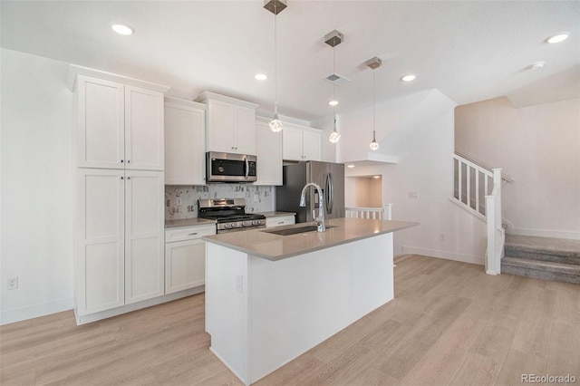 kitchen with pendant lighting, sink, appliances with stainless steel finishes, a kitchen island with sink, and white cabinetry