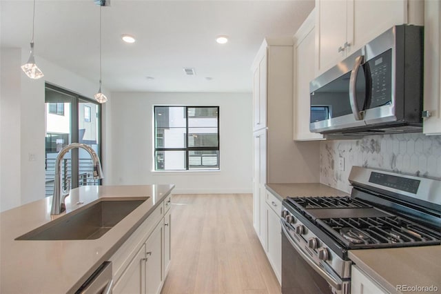 kitchen featuring sink, white cabinetry, hanging light fixtures, stainless steel appliances, and backsplash