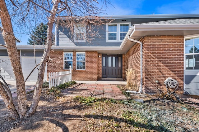 property entrance featuring an attached garage, fence, and brick siding