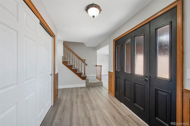 entrance foyer featuring light wood-type flooring, baseboards, stairway, and a textured ceiling