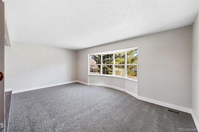 empty room featuring a textured ceiling, dark carpet, and baseboards