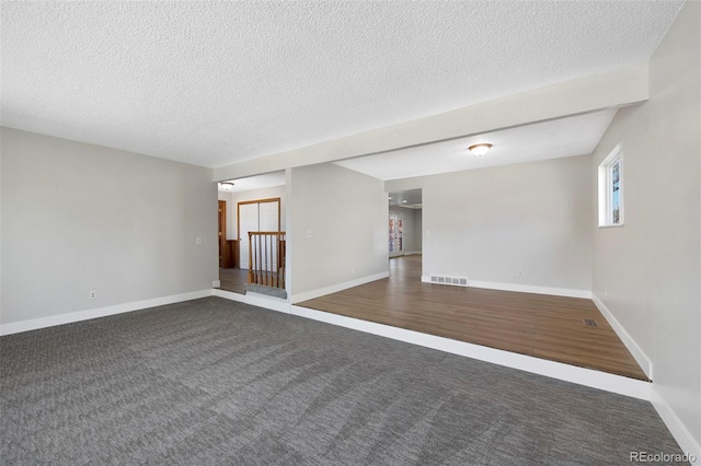 carpeted empty room featuring visible vents, a textured ceiling, and baseboards