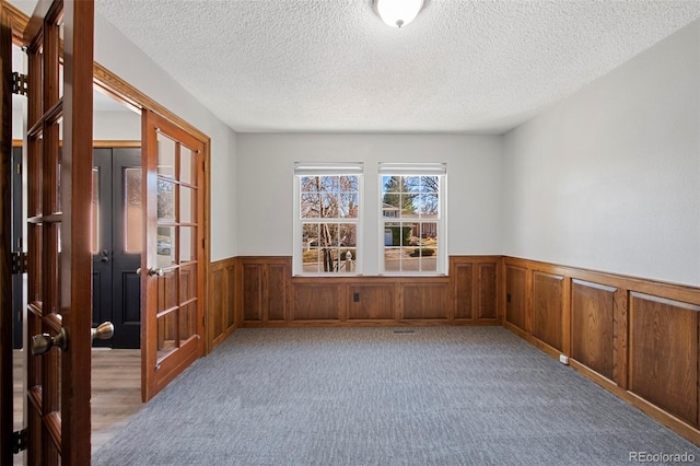 carpeted empty room featuring a textured ceiling, french doors, and wainscoting