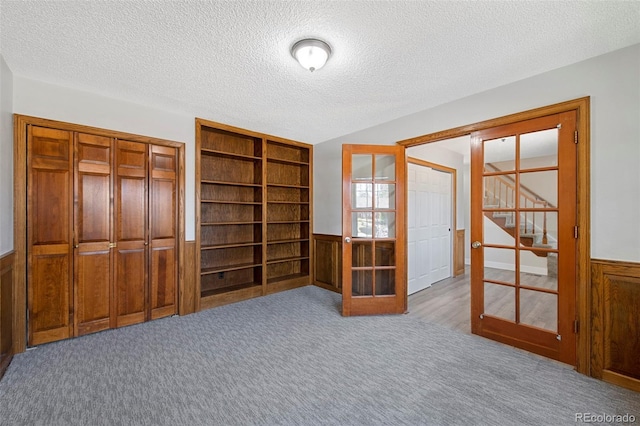 unfurnished room with a textured ceiling, a wainscoted wall, stairs, french doors, and carpet