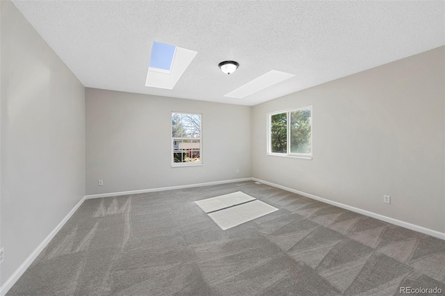 carpeted spare room featuring a skylight, baseboards, and a textured ceiling