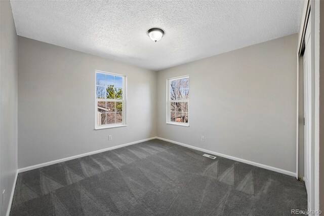 spare room featuring a textured ceiling, dark carpet, visible vents, and baseboards