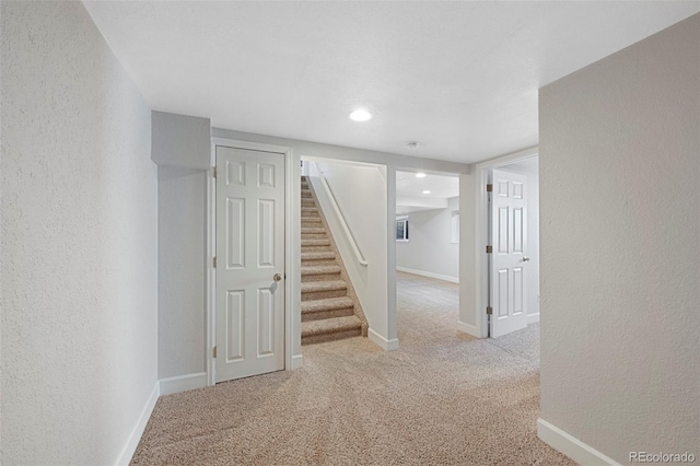 hallway with carpet flooring, a textured wall, baseboards, and stairs