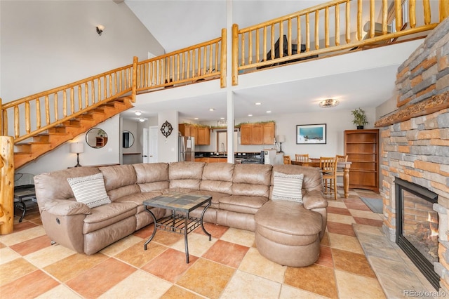 living area with stairway, a stone fireplace, and a towering ceiling