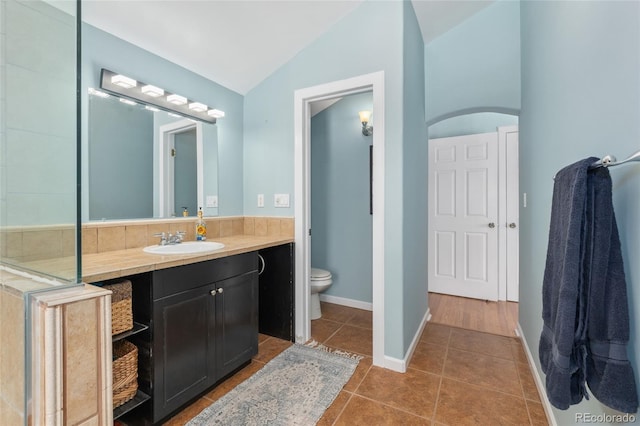 bathroom with tile patterned floors, toilet, lofted ceiling, baseboards, and vanity