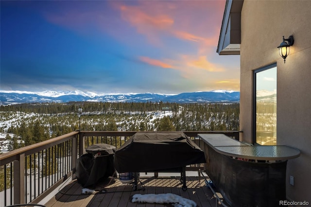 snow covered deck featuring a mountain view and a wooded view