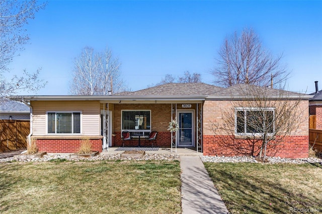 view of front of home featuring brick siding, covered porch, a front lawn, and fence