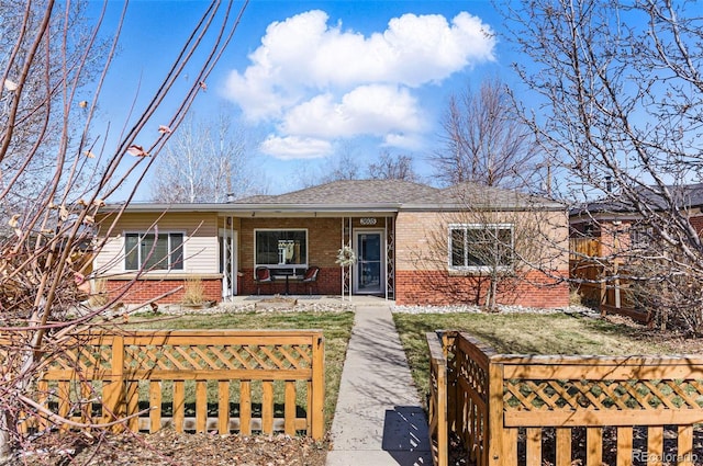 ranch-style home featuring brick siding, a porch, a shingled roof, and a fenced front yard