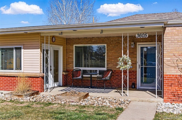 doorway to property with covered porch, brick siding, and roof with shingles