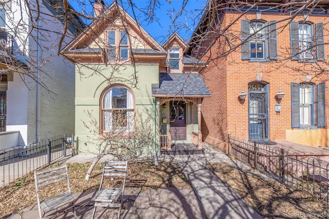 view of front of house featuring a fenced front yard, a shingled roof, brick siding, stucco siding, and a chimney