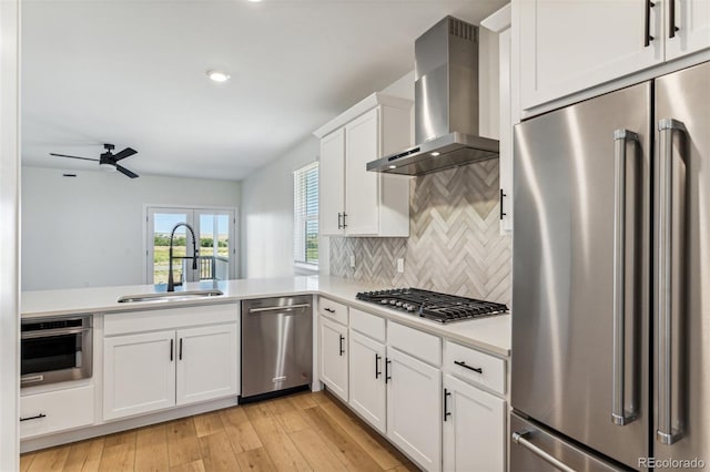 kitchen with light countertops, appliances with stainless steel finishes, a sink, light wood-type flooring, and wall chimney exhaust hood