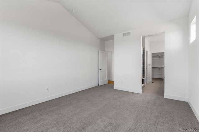 unfurnished bedroom featuring carpet, a walk in closet, baseboards, and high vaulted ceiling