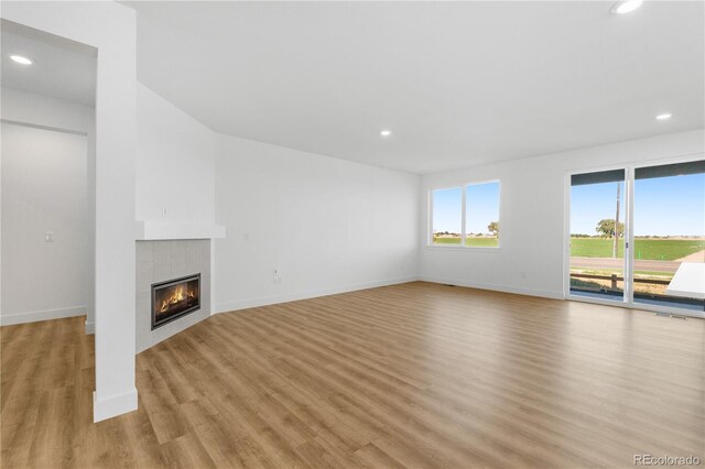 unfurnished living room with light wood-style flooring, a tile fireplace, recessed lighting, and baseboards