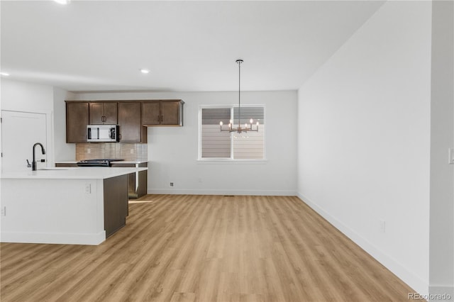 kitchen with appliances with stainless steel finishes, light wood-style flooring, light countertops, a sink, and dark brown cabinets