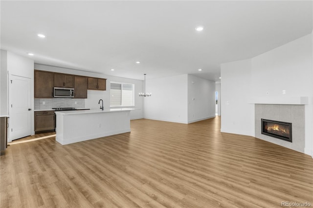 unfurnished living room with light wood-style flooring, recessed lighting, a tile fireplace, a sink, and baseboards