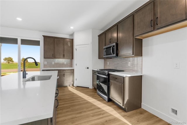 kitchen with stainless steel appliances, a sink, dark brown cabinets, light wood-style flooring, and decorative backsplash