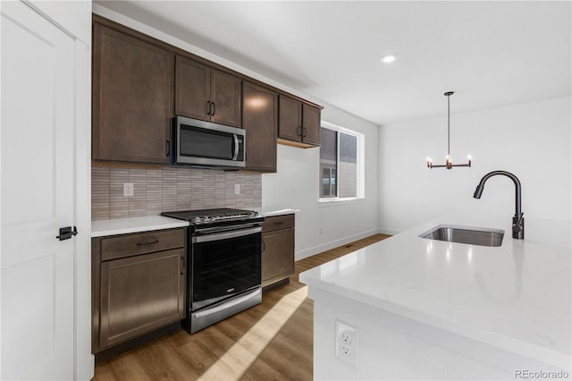 kitchen with stainless steel appliances, a sink, dark brown cabinets, wood finished floors, and tasteful backsplash
