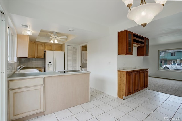 kitchen featuring a sink, white refrigerator with ice dispenser, stacked washer and clothes dryer, visible vents, and ceiling fan