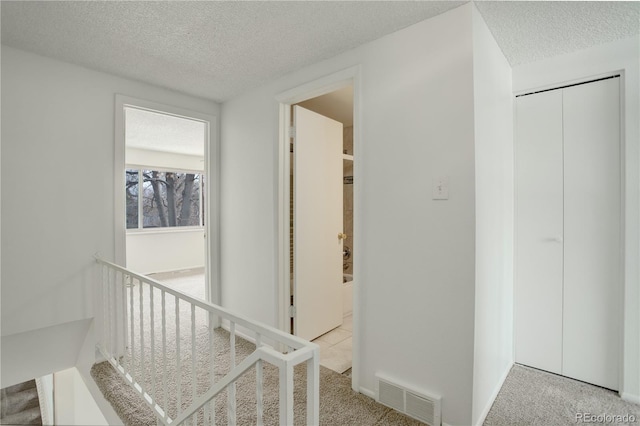 corridor with carpet floors, a textured ceiling, and visible vents