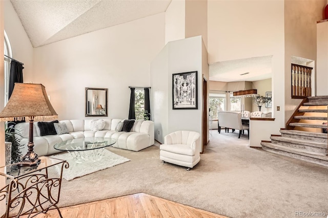 carpeted living room featuring stairway, high vaulted ceiling, and a textured ceiling