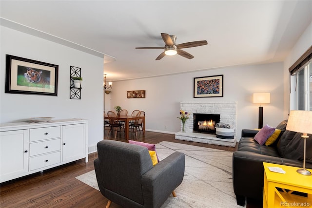 living room featuring baseboards, dark wood-type flooring, a fireplace, and ceiling fan with notable chandelier